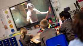 Primary school children watch a National Theatre production on a smart board in a classroom.