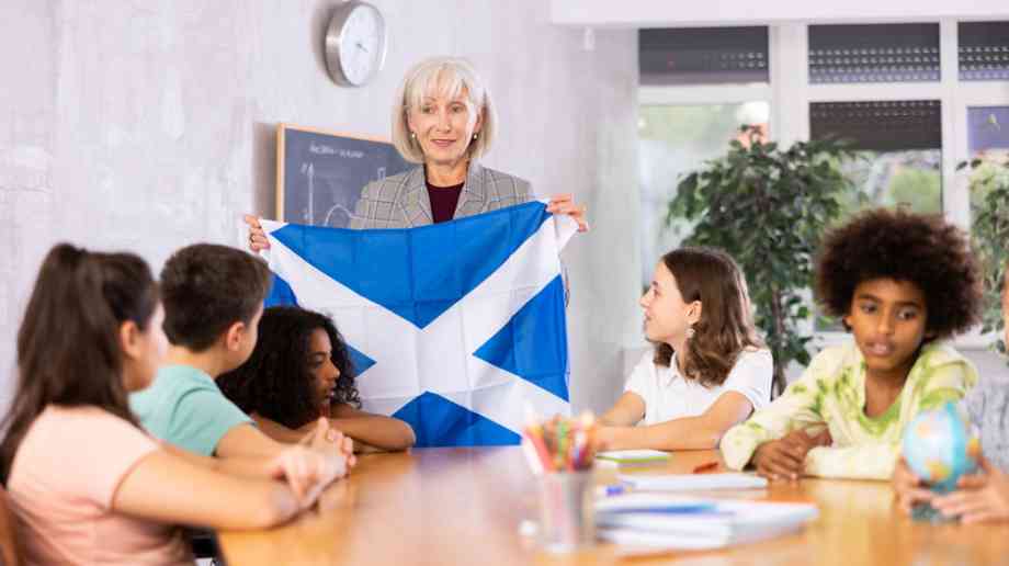 Teacher holds up Scottish flag to children.