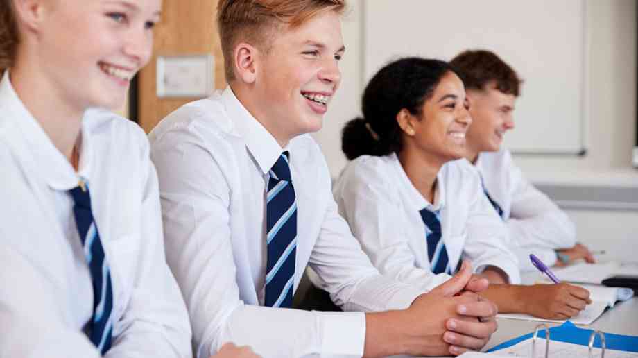 Secondary students sat at a desk in a row.