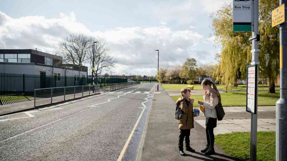 Two school children wait by a bus stop.