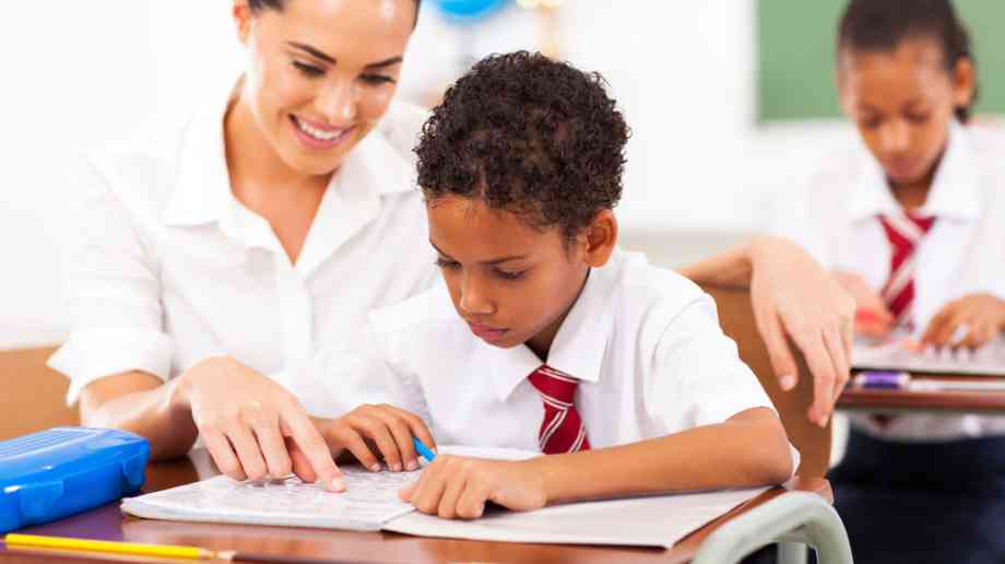 Young boy receives support from his teacher in a lesson.